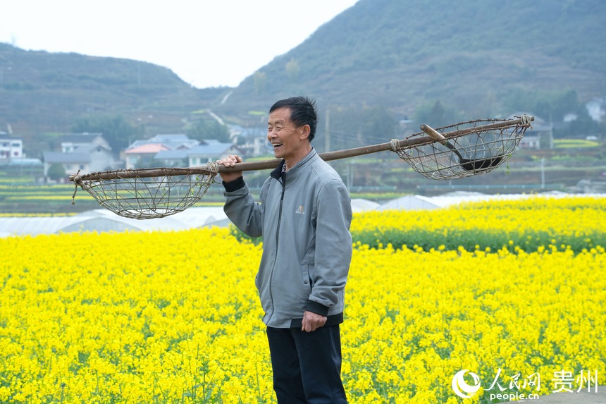 村民扛著農(nóng)具走在油菜花田中。人民網(wǎng) 陽茜攝