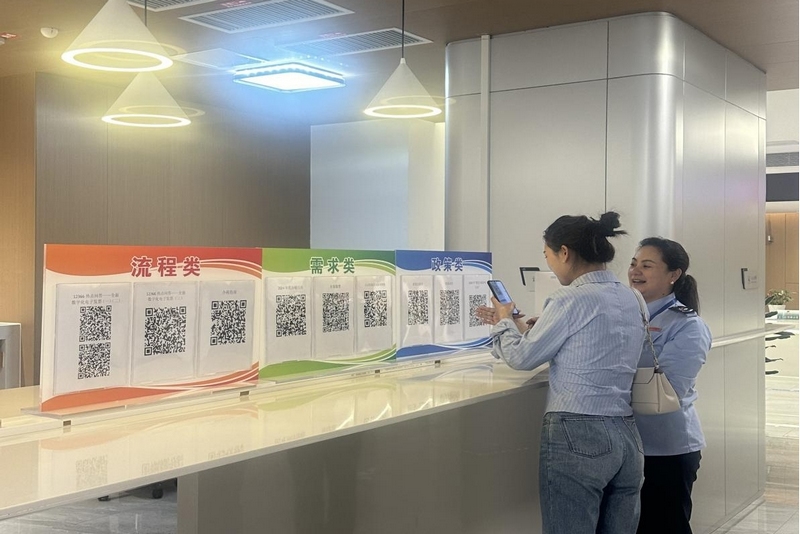 1圖為辦稅服務(wù)廳工作人員向納稅人介紹春風(fēng)“碼”上來展牌。
